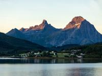 Ortschaft im Holandsfjord im Schatten und Felsspitzen im ersten Sonnenlicht